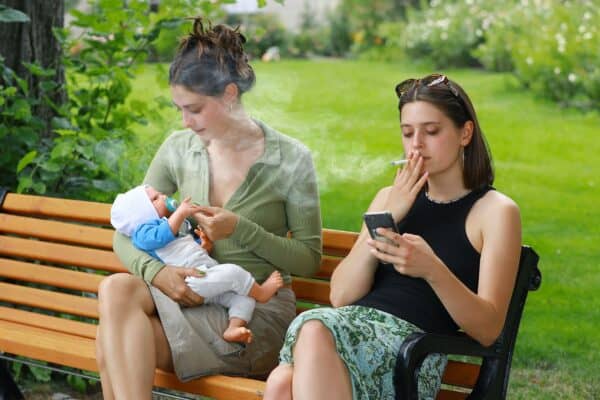 Mujer fumando junto a una madre y su bebé, ejemplo de exposición al humo de segunda mano
