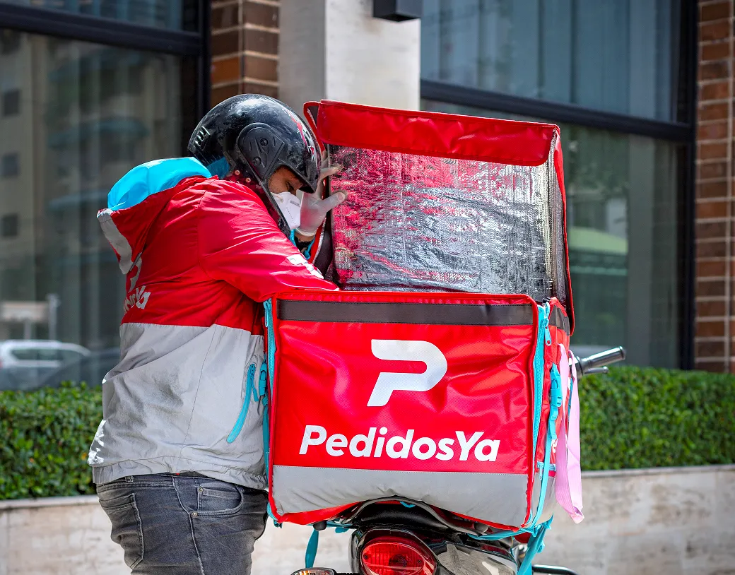 Repartidor de PedidosYa en motocicleta realizando una entrega, en referencia a la adquisición de Delivery Hero por parte de Uber.