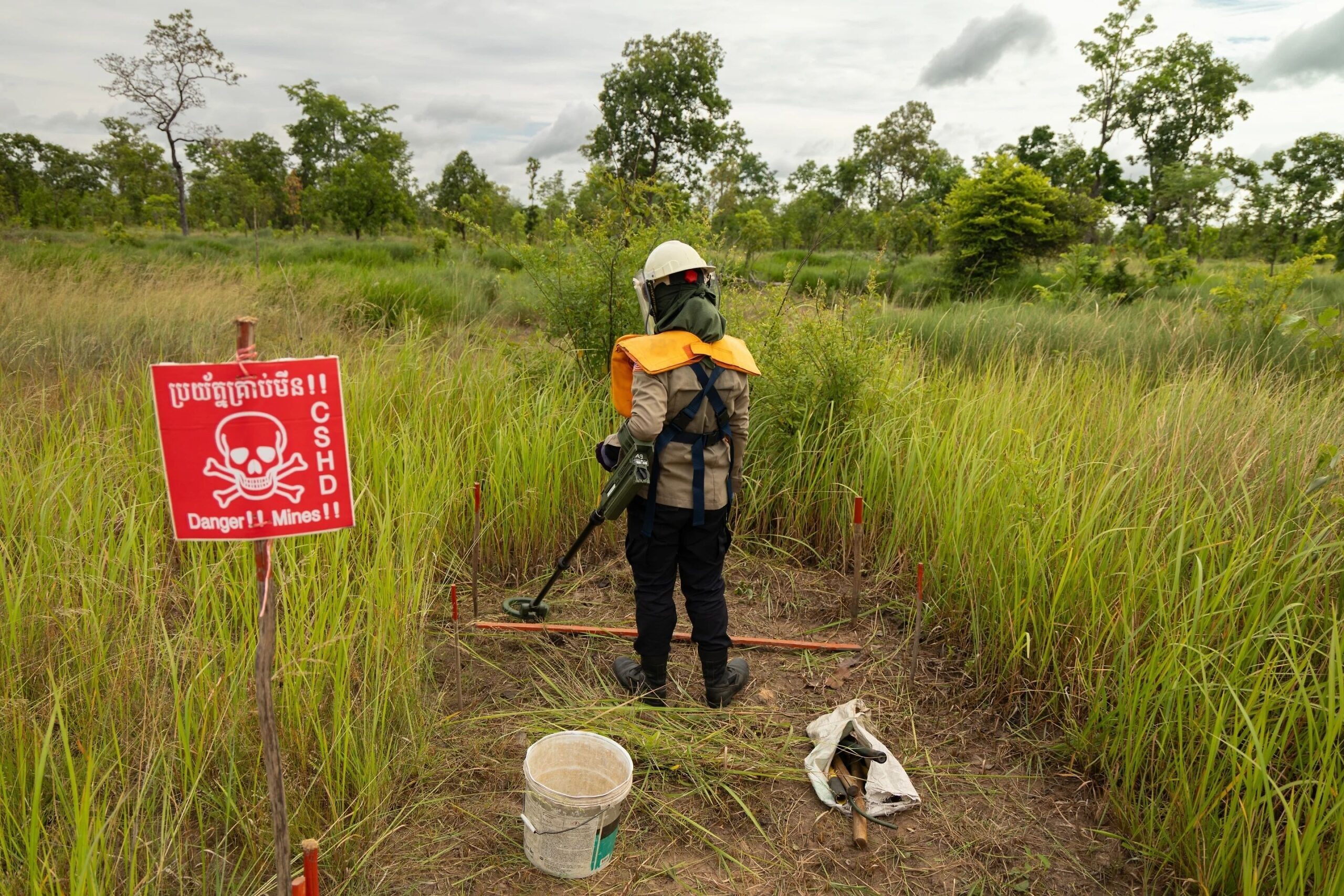 Un desminador trabaja en un campo de minas en Camboya, junto a un cartel de advertencia sobre el peligro de explosivos.
