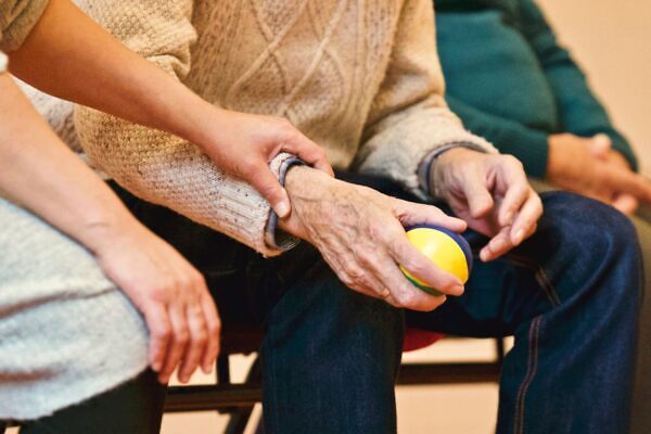 Una persona anciana recibe apoyo de un cuidador, tomando las manos en interiores, mostrando compasión.