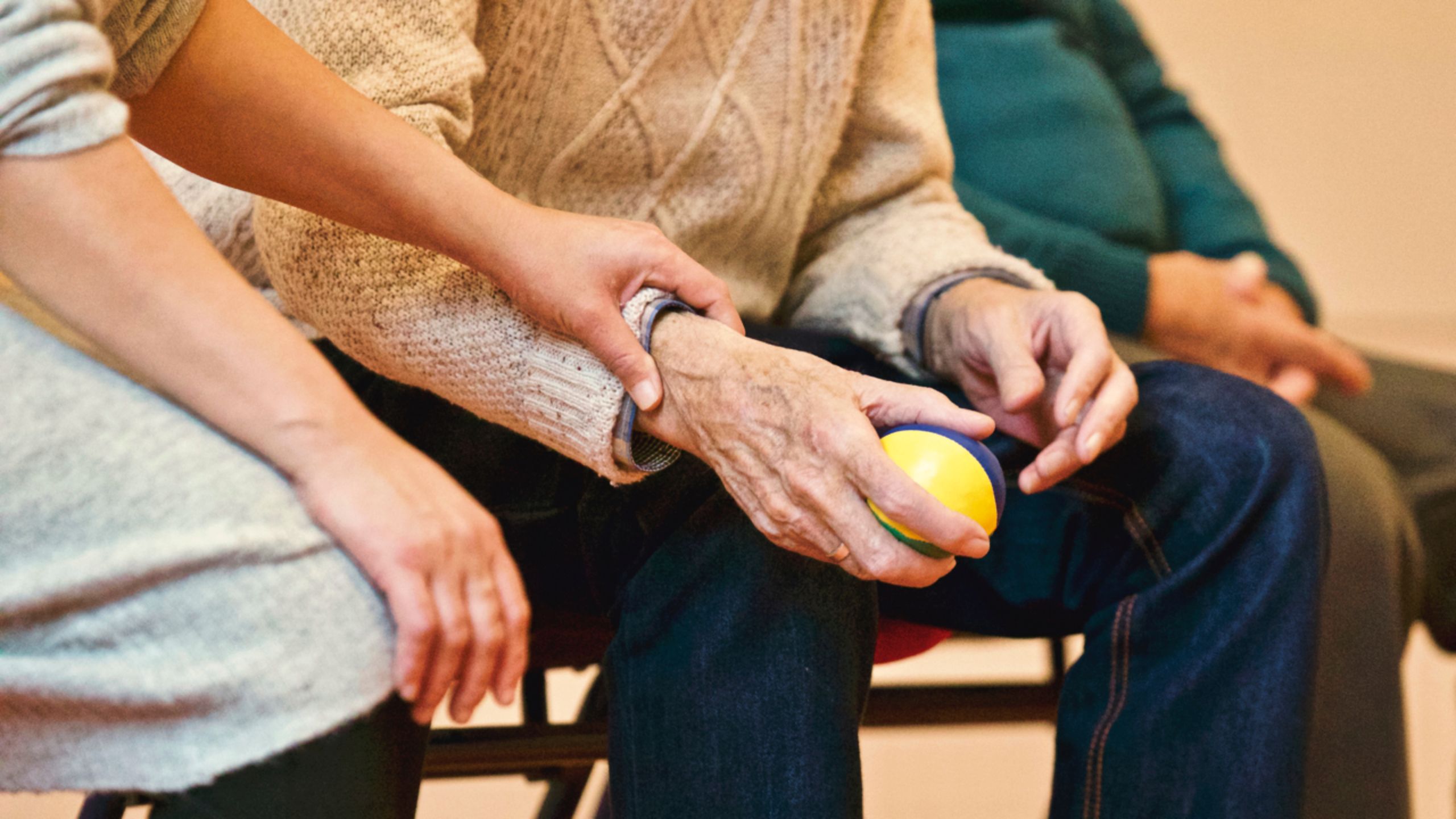 Una persona anciana recibe apoyo de un cuidador, tomando las manos en interiores, mostrando compasión.