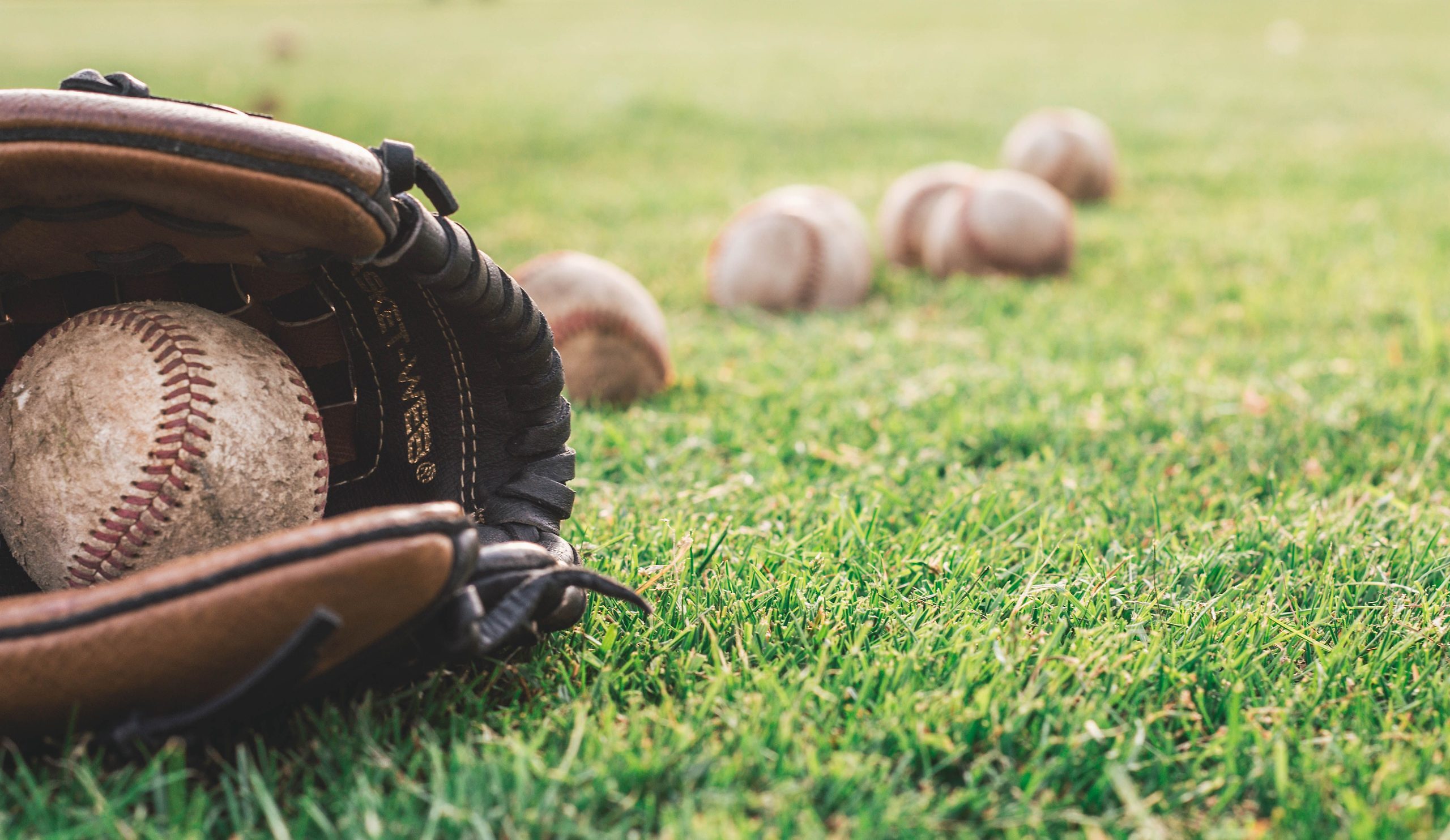 Guante de béisbol con una pelota y varias pelotas en el césped, simbolizando el inicio de la temporada 2026-2027.