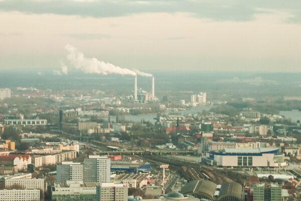 Vista aérea que muestra un horizonte urbano con chimeneas industriales emitiendo humo, bajo un cielo apagado.