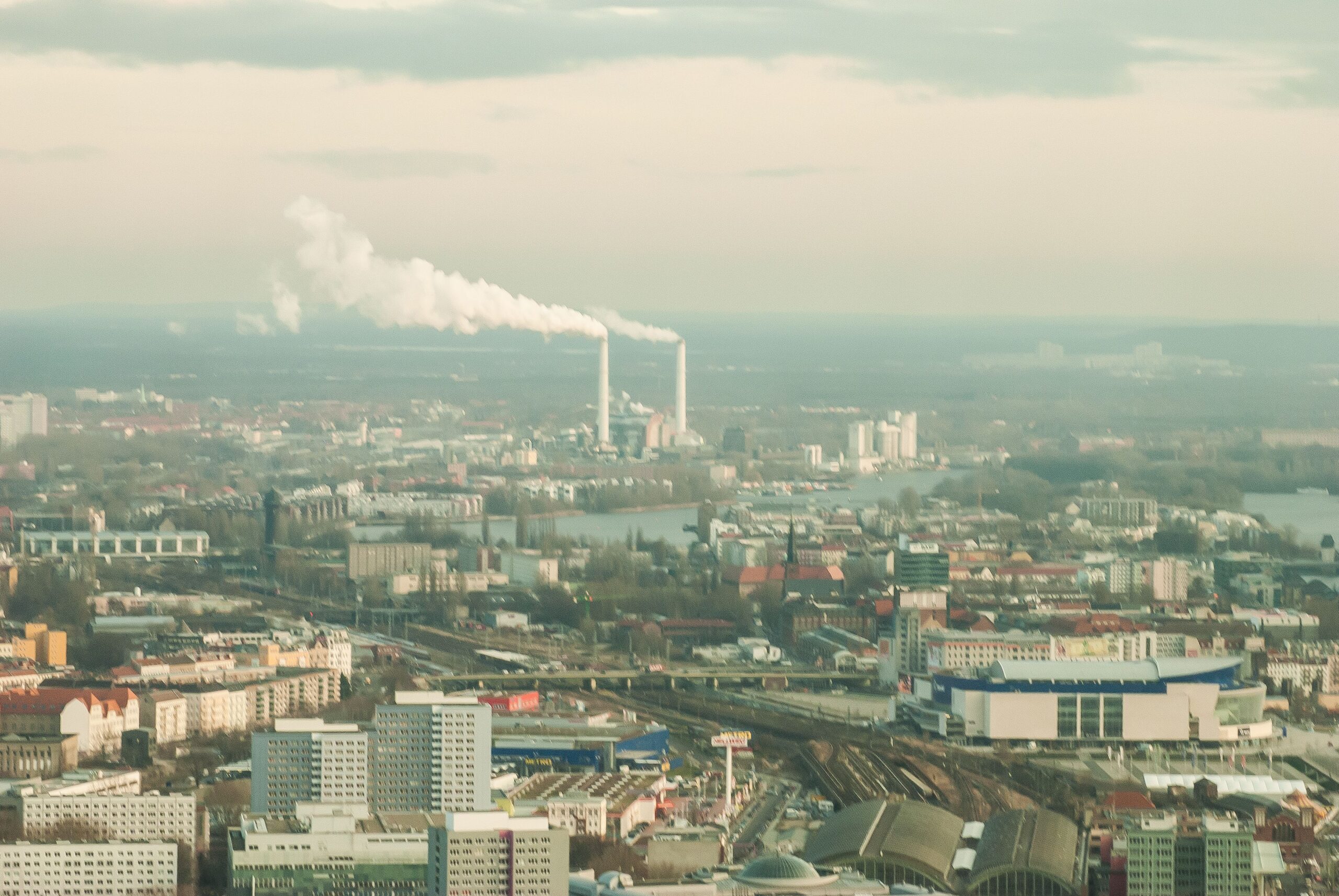 Vista aérea que muestra un horizonte urbano con chimeneas industriales emitiendo humo, bajo un cielo apagado.