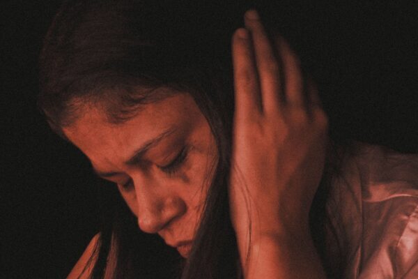 Una mujer en profunda reflexión, cubriéndose los oídos en un ambiente tenue, destacando la introspección.
