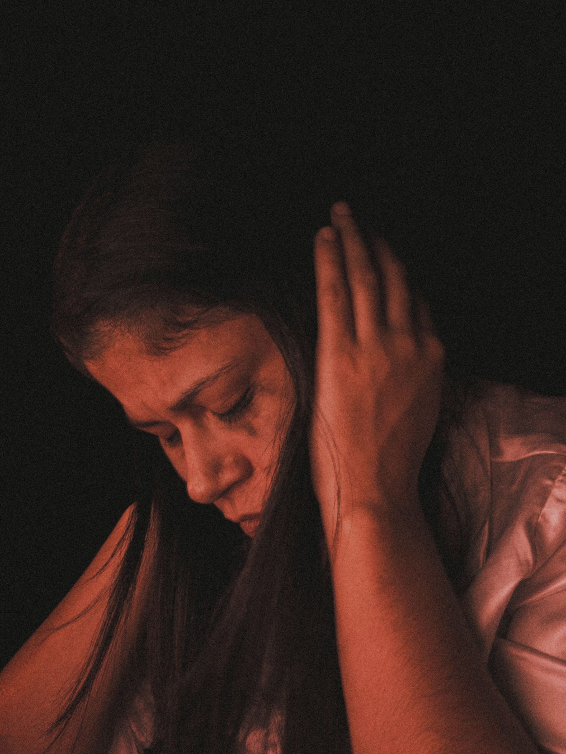 Una mujer en profunda reflexión, cubriéndose los oídos en un ambiente tenue, destacando la introspección.