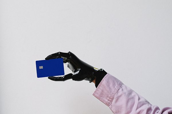 Una mano prostética con una camisa rosa sosteniendo una tarjeta azul contra un fondo blanco, mostrando tecnología y diseño moderno.